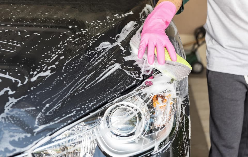 Someone washing a dark car by hand with soap and a sponge